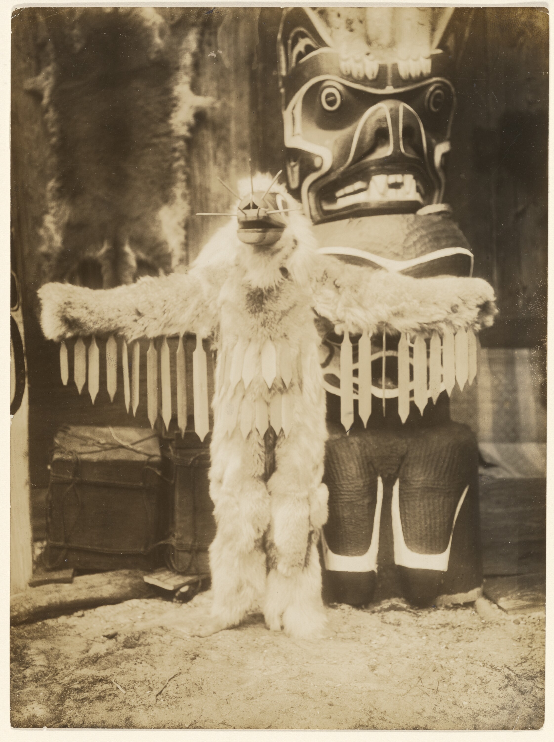 Edward Curtis, "A vespa com seu zumbido vai espantar todos", homem Kwakiutl vestido de animal em frente a um totem c. 1910–14. Fotografia. The J. Paul Getty Museum, Los Angeles, 84.XM.638.49. Domínio público.